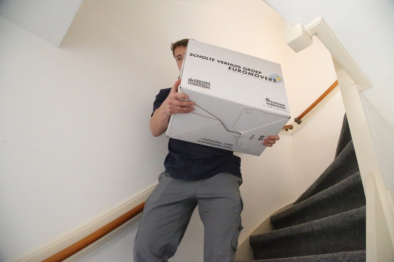 SVG-verhuizer draagt een verhuisdoos over de trap in een woning